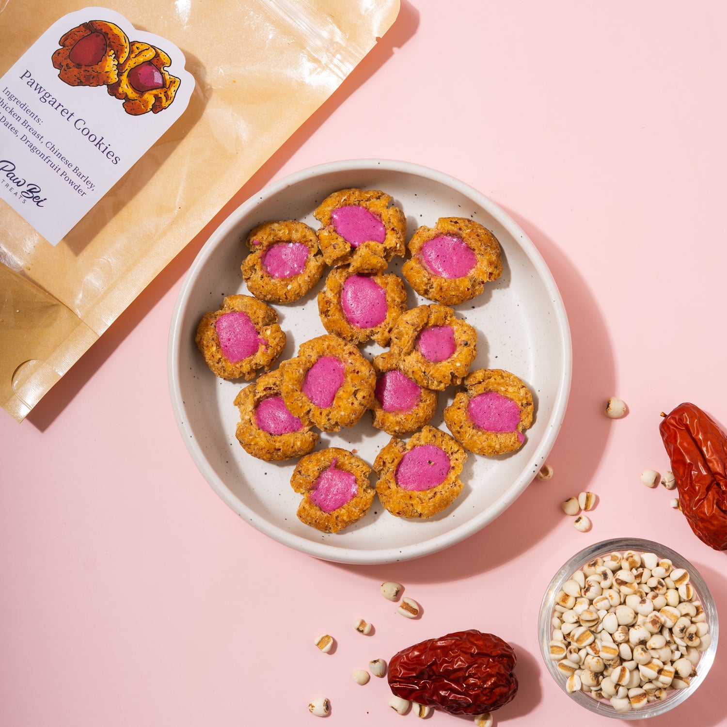 Cookies with pink centers on a plate, surrounded by ingredients on a pink background