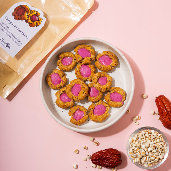 Cookies with pink centers on a plate, surrounded by ingredients on a pink background