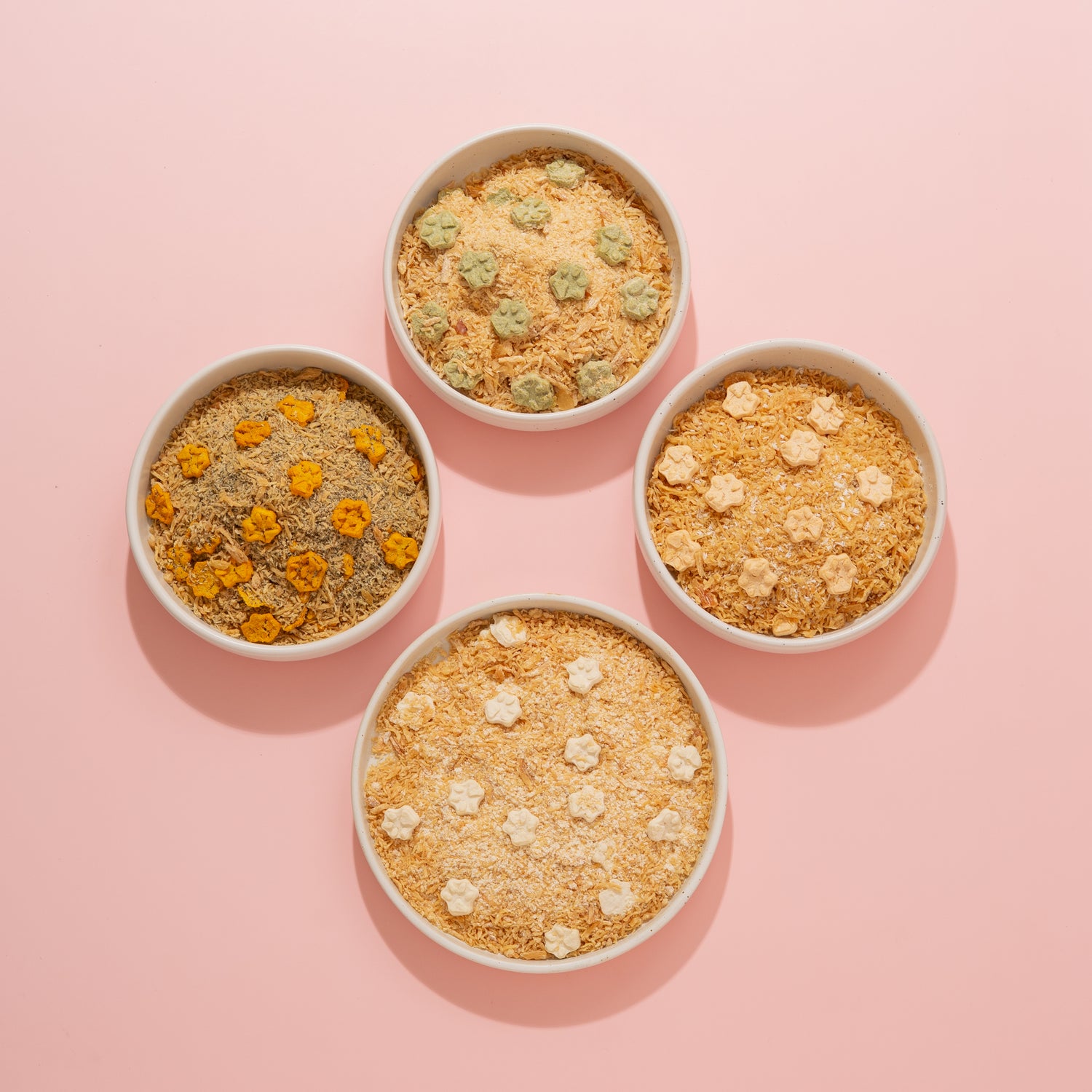 Four bowls of different types of pet food on a pink background